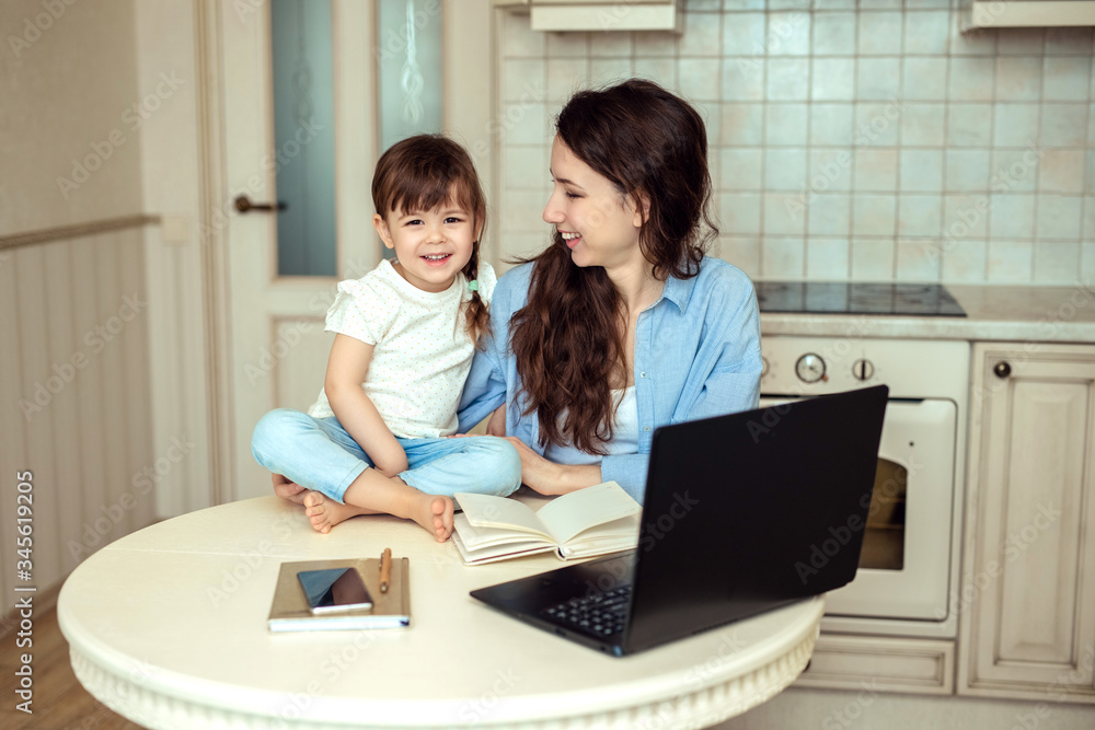 freelance work at home. happy woman at laptop next to small child in kitchen freelance work at home. happy woman at laptop next to small child in kitchen