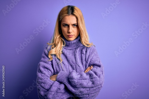 Young beautiful blonde woman wearing casual turtleneck sweater over purple background skeptic and nervous, disapproving expression on face with crossed arms. Negative person. © Krakenimages.com