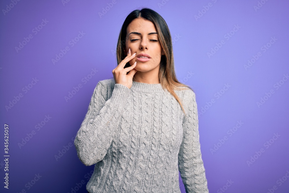 Young beautiful woman wearing casual sweater standing over isolated purple background touching mouth with hand with painful expression because of toothache or dental illness on teeth. Dentist Young beautiful woman wearing casual sweater standing over isolated purple background touching mouth with hand with painful expression because of toothache or dental illness on teeth. Dentist