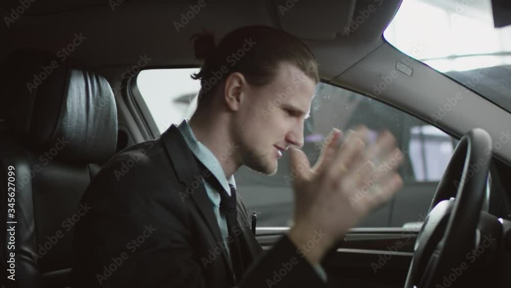 Right sight view of angry man is shouting sitting in the car on a driver's seat and using his phone. Businessman yelling while driving a car. Right sight view of angry man is shouting sitting in the car on a driver's seat and using his phone. Businessman yelling while driving a car.