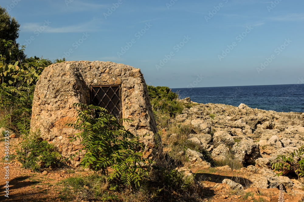 Mediterranean landscape of Sicily, Italy. View shot in Zingaro Nature Reserve. In the background old stone hut/house. Mix of rock, coast, azur water, plants, flora, architecture and sky.