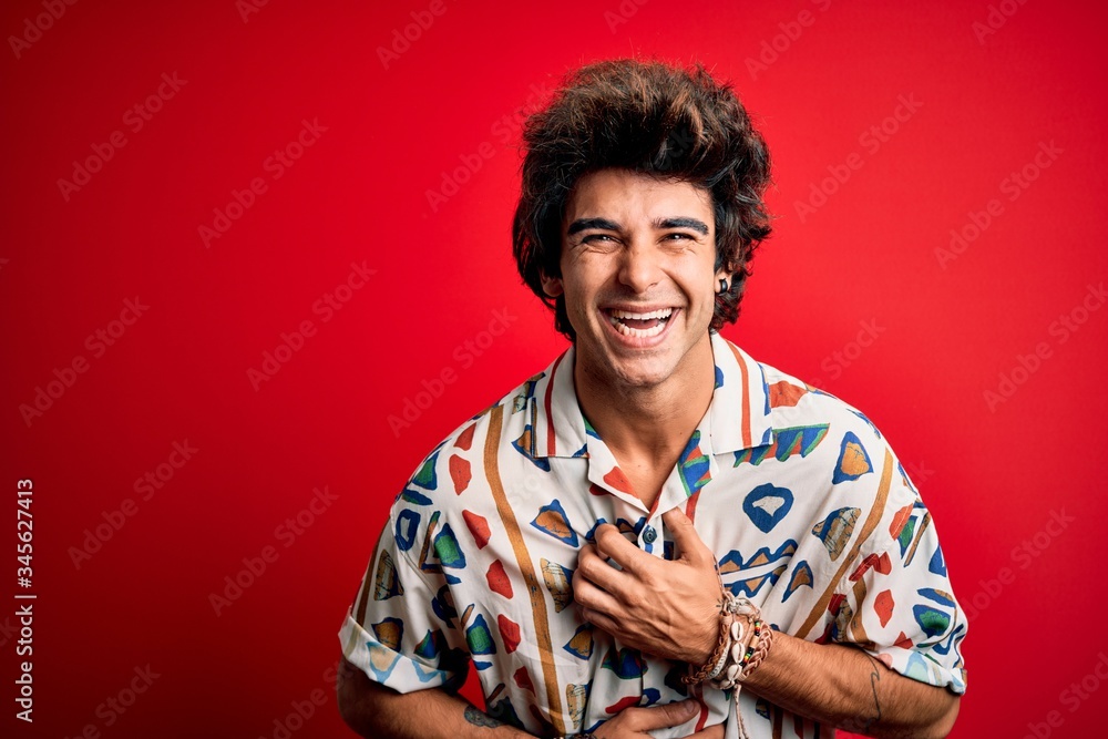 Young handsome man on vacation wearing summer shirt over isolated red background smiling and laughing hard out loud because funny crazy joke with hands on body. Young handsome man on vacation wearing summer shirt over isolated red background smiling and laughing hard out loud because funny crazy joke with hands on body.