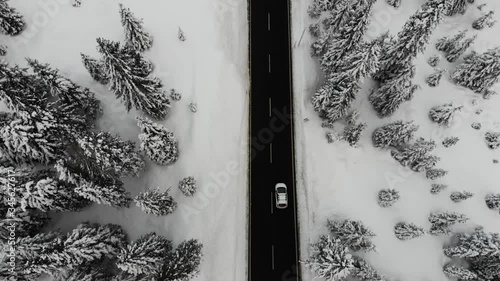 Aerial shot of white car driving on narrow road through snowy landscape