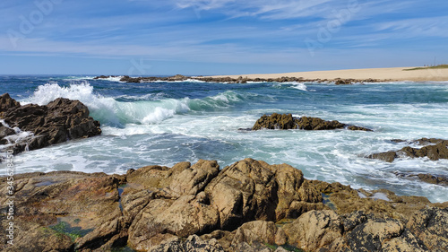 Waves breaking over rocks at beach on bright sunny summer day in Povoa de Varzim, Portugal
