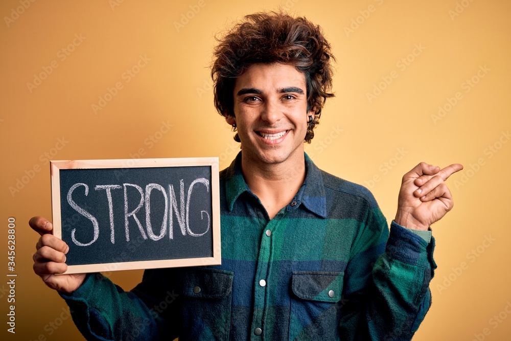 Young handsome man holding blackboard with strong word over isolated yellow background very happy pointing with hand and finger to the side Young handsome man holding blackboard with strong word over isolated yellow background very happy pointing with hand and finger to the side
