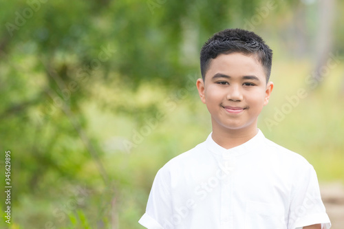A portrait of a good looking Asian boy wearing a white shirt smiling in a park.