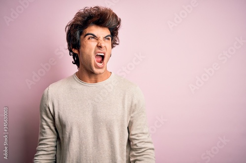 Young handsome man wearing casual t-shirt standing over isolated pink background angry and mad screaming frustrated and furious, shouting with anger. Rage and aggressive concept.