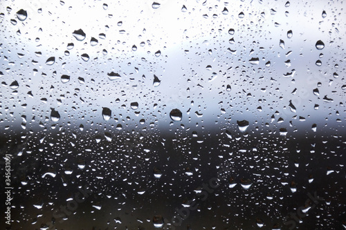 Drops of morning summer rain on the transparent window of the house on a blurred background of nature. Summer vacation and travel concept