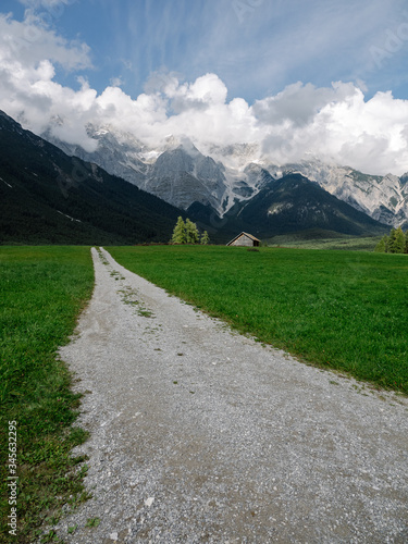 View on Tyrol mountains with green meadow and a gravelly path leading towards the mountains. With partly cloudy sky.