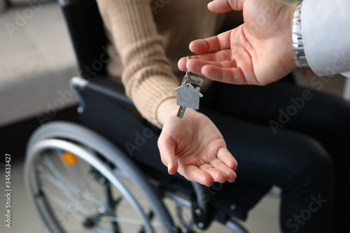 Close-up of realtor putting keys from new apartment on owners hand. Person sitting in wheelchair. Disabled people. Buy property. Real estate and mortgage concept