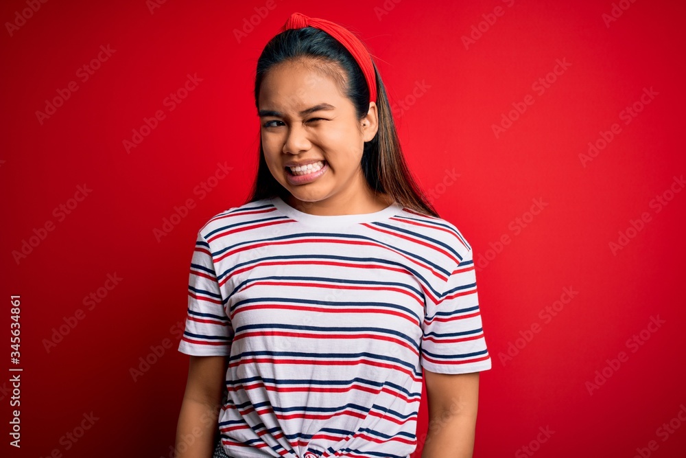 Young beautiful asian girl wearing casual striped t-shirt over isolated red background winking looking at the camera with sexy expression, cheerful and happy face. Young beautiful asian girl wearing casual striped t-shirt over isolated red background winking looking at the camera with sexy expression, cheerful and happy face.