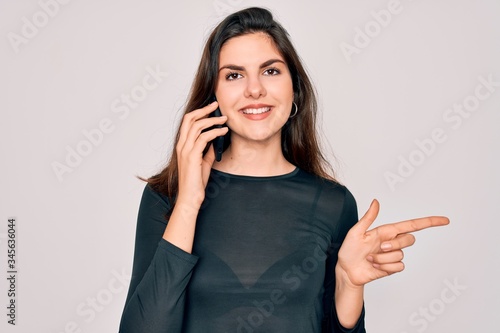 Young beautiful woman having a conversation talking on smartphone ove isolated background very happy pointing with hand and finger to the side