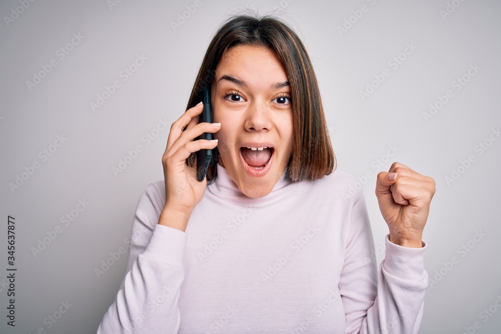 Beautiful brunette girl having conversation talking on the smartphone over white background screaming proud and celebrating victory and success very excited, cheering emotion Beautiful brunette girl having conversation talking on the smartphone over white background screaming proud and celebrating victory and success very excited, cheering emotion