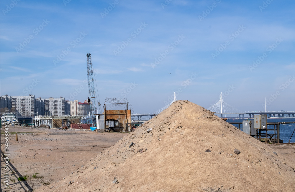 A pile of sand on the construction or repair site against the background of equipment and houses of typical building. Horizontal orientation, selective focus. A pile of sand on the construction or repair site against the background of equipment and houses of typical building. Horizontal orientation, selective focus.