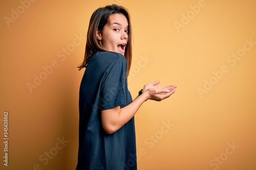 Young beautiful brunette girl doing volunteering wearing t-shirt with volunteer message word pointing aside with hands open palms showing copy space, presenting advertisement smiling excited happy