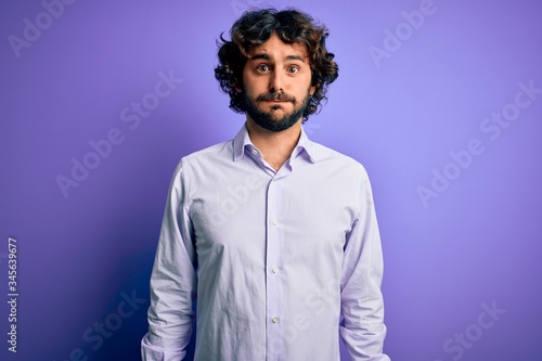 Young handsome business man with beard wearing shirt standing over purple background puffing cheeks with funny face. Mouth inflated with air, crazy expression.