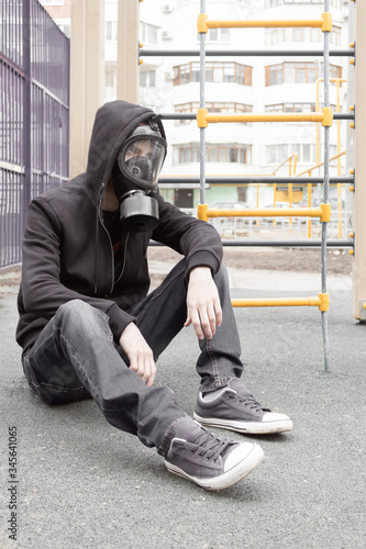 A lonely man in a respiratory mask sits on a ground on a deserted city during a coronavirus epidemic in beautiful spring time. Russia, Samara, april. Selective and soft focus.