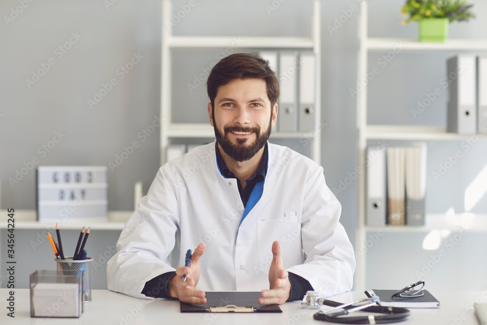 Smiling bearded medical doctor sitting in a hospital.