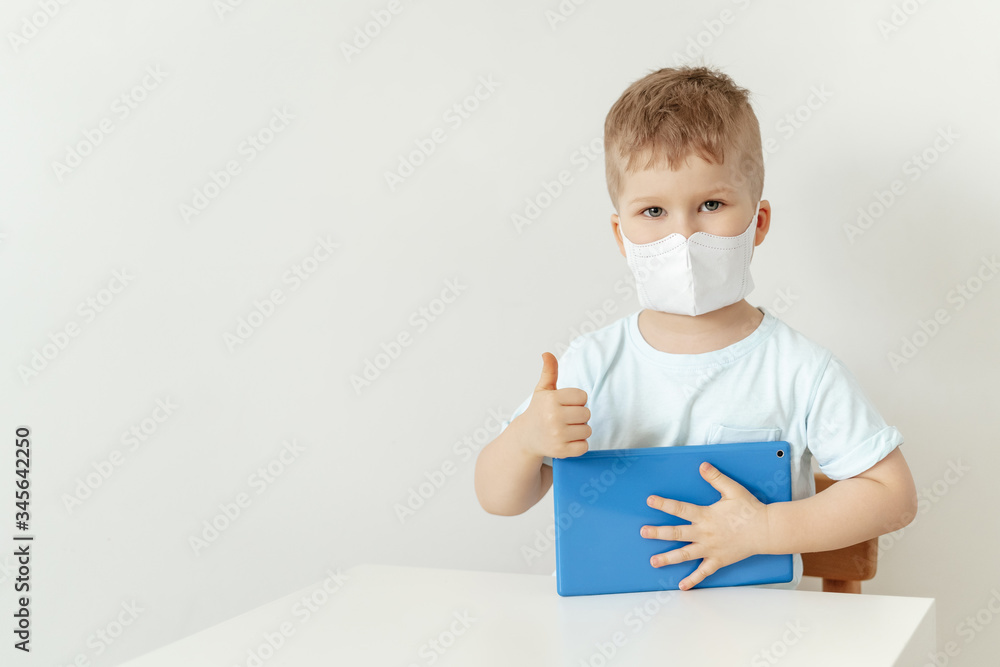 Caucasian Boy Wearing Mask Sitting with Tablet. Cute Toddler Showing Thumb up Sign, Holding Laptop. Child in Flu Protection Looking at Camera. Coronavirus Quarantine, Indoors Isolation Concept Caucasian Boy Wearing Mask Sitting with Tablet. Cute Toddler Showing Thumb up Sign, Holding Laptop. Child in Flu Protection Looking at Camera. Coronavirus Quarantine, Indoors Isolation Concept