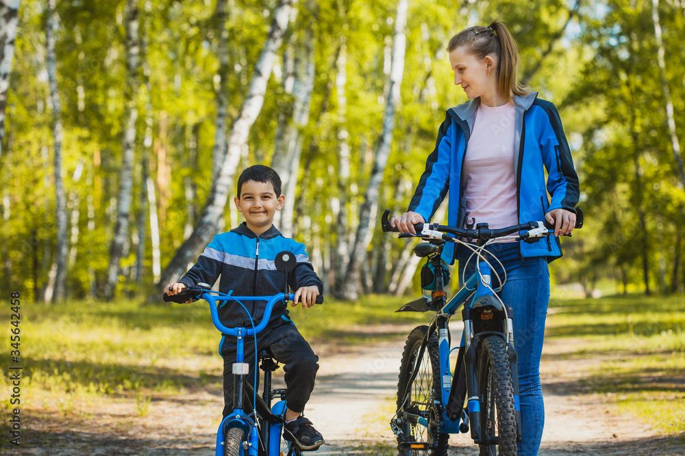 Fototapeta premium Funny boy cyclistrides a bike with mom in the sunny forest on a bike. Adventure travel.