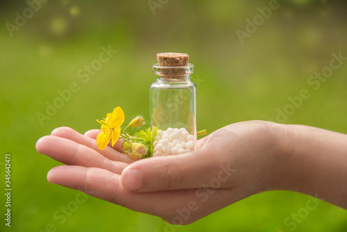 glass container with homeopathic granules and a flower in the palm of your hand. beautiful natural background