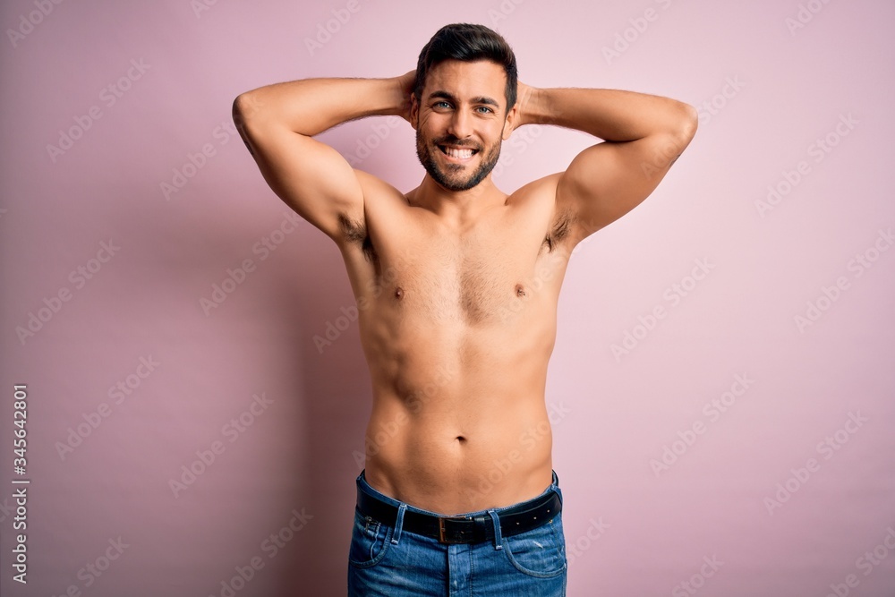Young handsome strong man with beard shirtless standing over isolated pink background relaxing and stretching, arms and hands behind head and neck smiling happy Young handsome strong man with beard shirtless standing over isolated pink background relaxing and stretching, arms and hands behind head and neck smiling happy