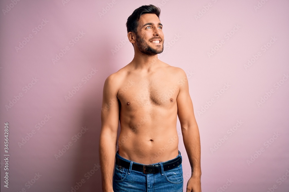 Fototapeta premium Young handsome strong man with beard shirtless standing over isolated pink background looking away to side with smile on face, natural expression. Laughing confident.