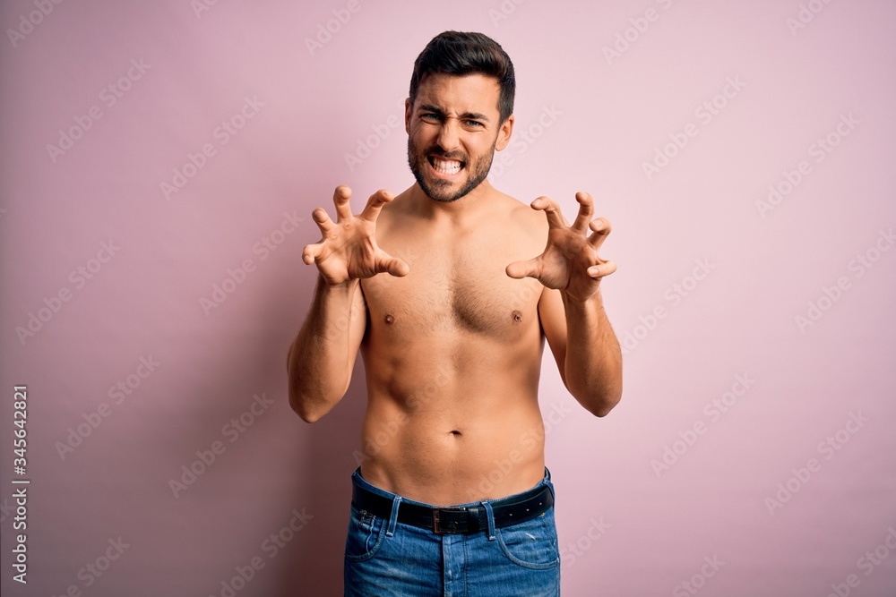 Young handsome strong man with beard shirtless standing over isolated pink background smiling funny doing claw gesture as cat, aggressive and sexy expression
