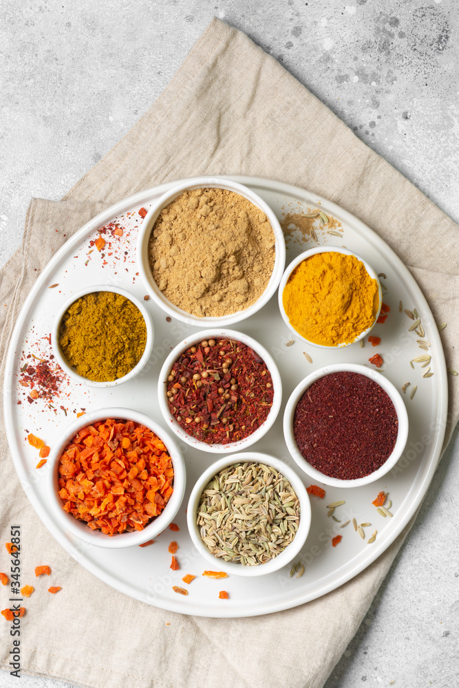 Spices in white bowls on a light gray table. Turmeric, ginger, curry, fennel and sumac in white bowls. Top view with space for text