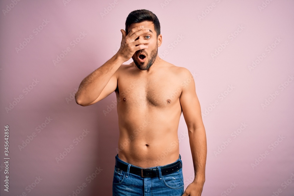 Young handsome strong man with beard shirtless standing over isolated pink background peeking in shock covering face and eyes with hand, looking through fingers with embarrassed expression. Young handsome strong man with beard shirtless standing over isolated pink background peeking in shock covering face and eyes with hand, looking through fingers with embarrassed expression.