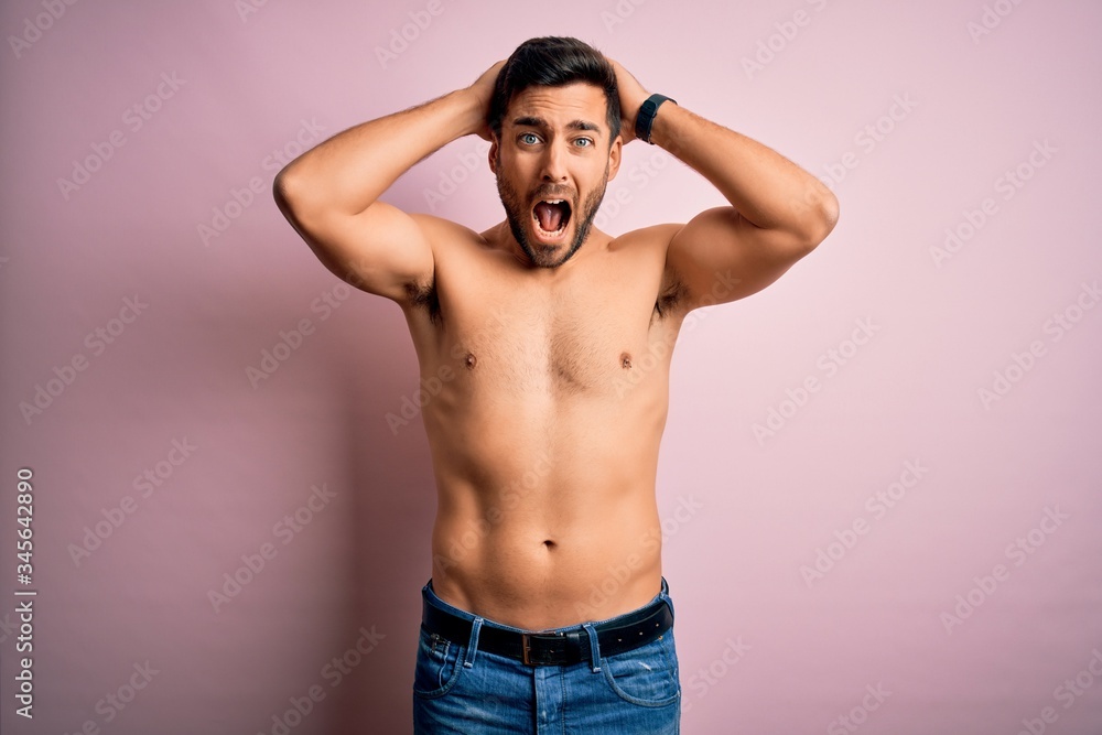 Young handsome strong man with beard shirtless standing over isolated pink background Crazy and scared with hands on head, afraid and surprised of shock with open mouth