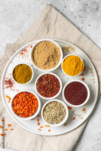 Spices in white bowls on a light gray table. Turmeric, ginger, curry, fennel and sumac in white bowls. Top view with space for text