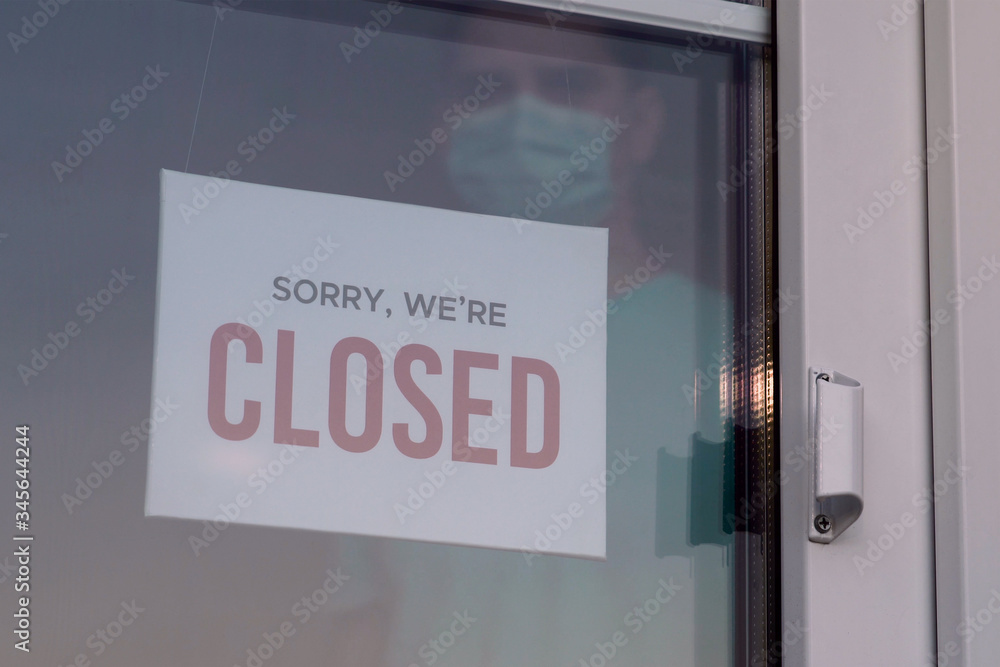 Business owner in medical mask puts a CLOSED sign Business owner in medical mask puts a CLOSED sign