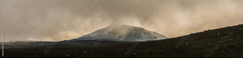 Etna volcano, Sicily, Italy. Mars-like or Moon-like mountain landscape, hiking in the clouds. Volcanic view panorama with peak in the background. A lot of mist, smoke, clouds, vapor. 