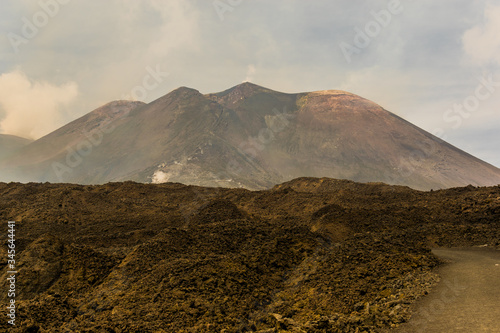 Etna volcano silhouette, Sicily, Italy. Mars-like or Moon-like mountain landscape. In the background view of main craters and peak of mountain. In the foreground moguls and road.