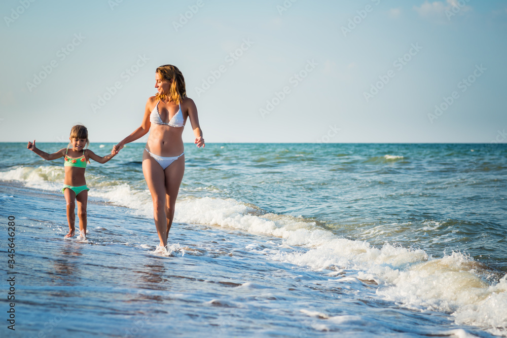 Young pretty mother and little daughter run on the sea shore during vacation on a sunny warm summer day against a blue sky. Concept vacation with children and wellness