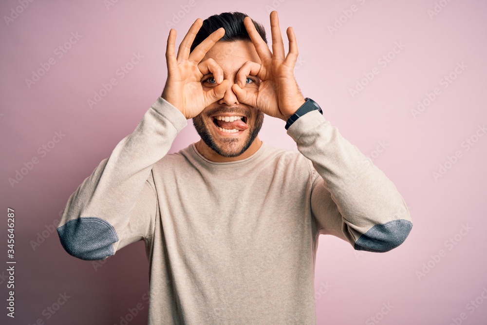 Young handsome man wearing casual sweater standing over isolated pink background doing ok gesture like binoculars sticking tongue out, eyes looking through fingers. Crazy expression. Young handsome man wearing casual sweater standing over isolated pink background doing ok gesture like binoculars sticking tongue out, eyes looking through fingers. Crazy expression.