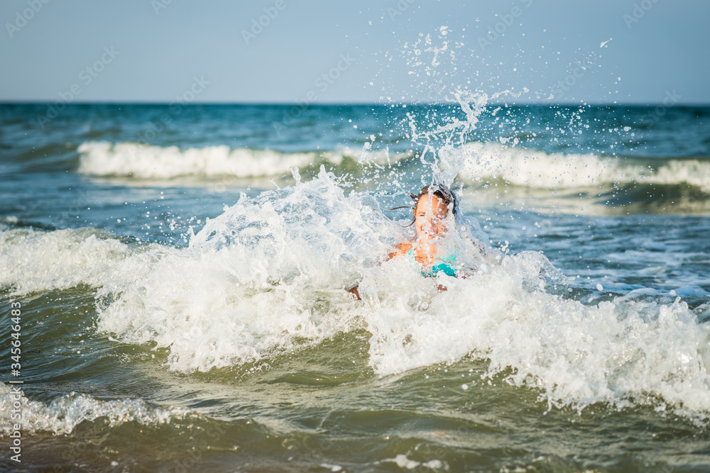 Happy emotional little girl bathes in the foamy stormy sea waves on a sunny warm summer day. The concept of long-awaited vacation and travel with children