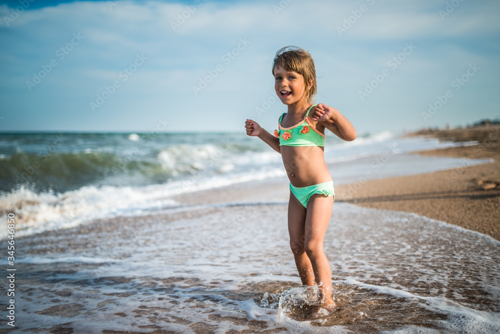 Naklejka premium Joyful little girl enjoys a beach day while relaxing at sea on a sunny warm summer day. Summer vacation and relaxation concept
