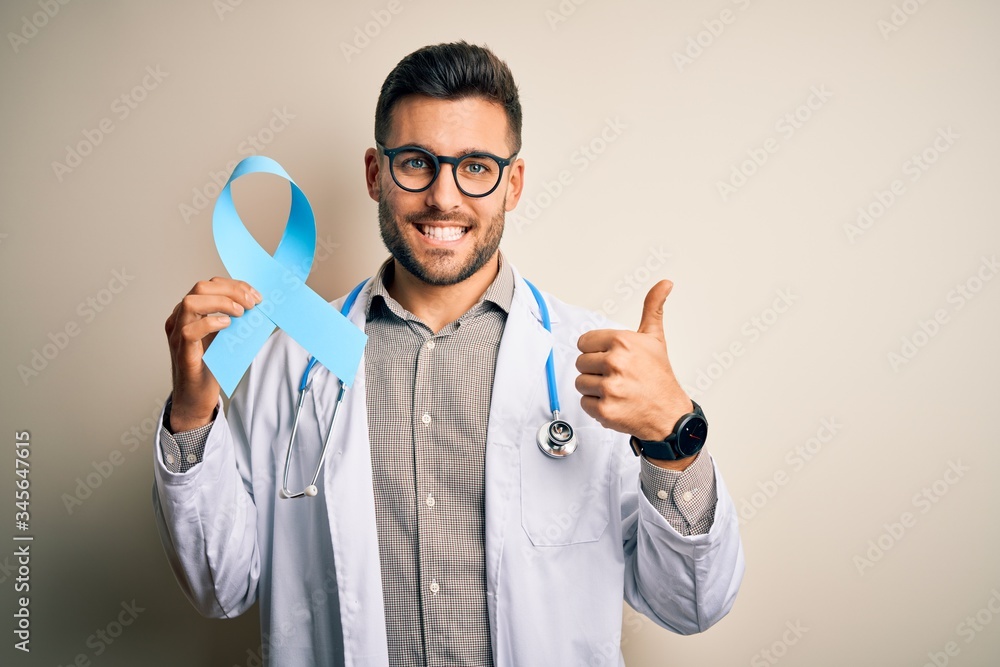 Naklejka premium Young professional doctor man holding colon awareness blue ribbon over isolated background happy with big smile doing ok sign, thumb up with fingers, excellent sign