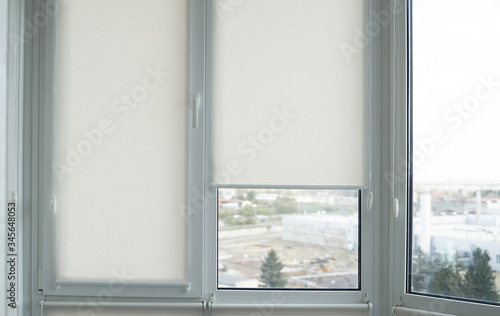 Details of white fabric roller blinds on the plastic window with wood texture in the living room.