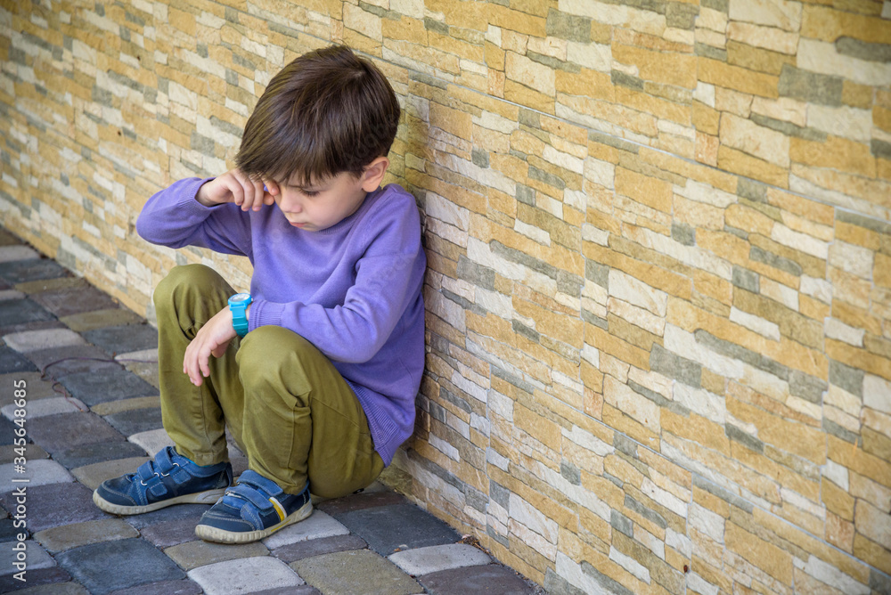 Little boy sad sitting alone at school hides his face. Isolation and bullying concept. Kid sad and unhappy, child was crying, upset, feel sick Little boy sad sitting alone at school hides his face. Isolation and bullying concept. Kid sad and unhappy, child was crying, upset, feel sick