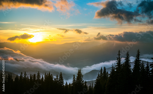 Bright sun setting behind mountains with dramatic sky on background