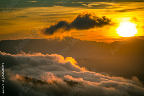Bright sun setting behind mountains with dramatic sky on background