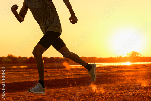 close up silhouette legs and feet of extreme cross country man running and training on rural track jogging at sunset with harsh sunlight and lens flare in countryside sport and healthy lifestyle