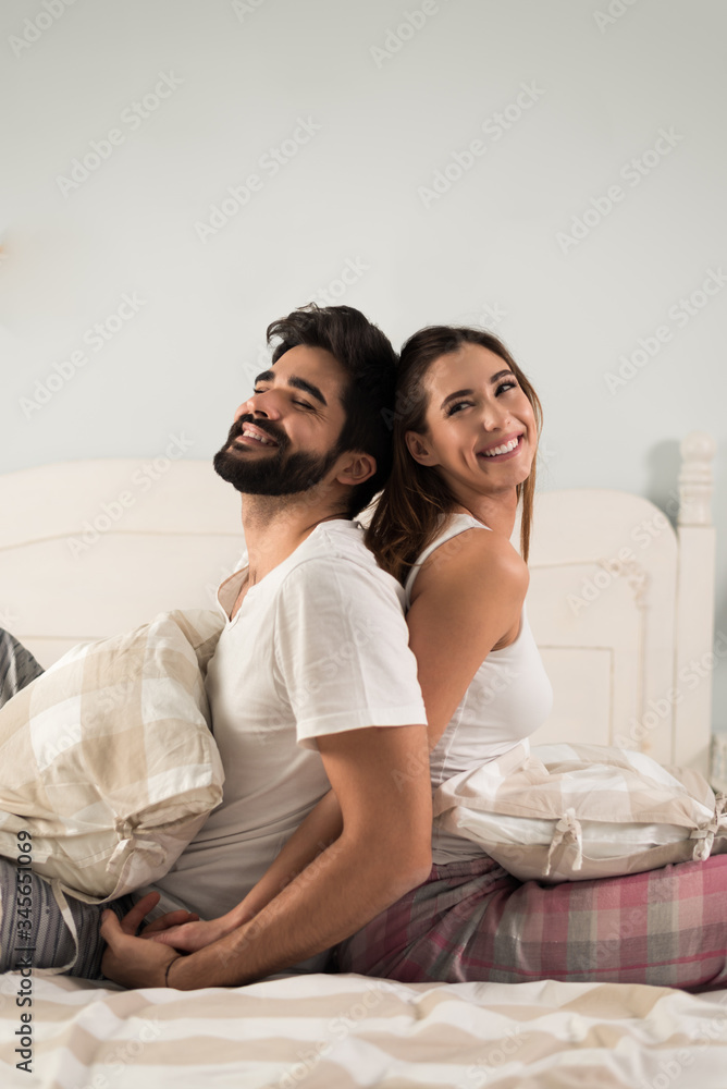 Cheerful couple having fun while sitting back to back in their bedroom Cheerful couple having fun while sitting back to back in their bedroom