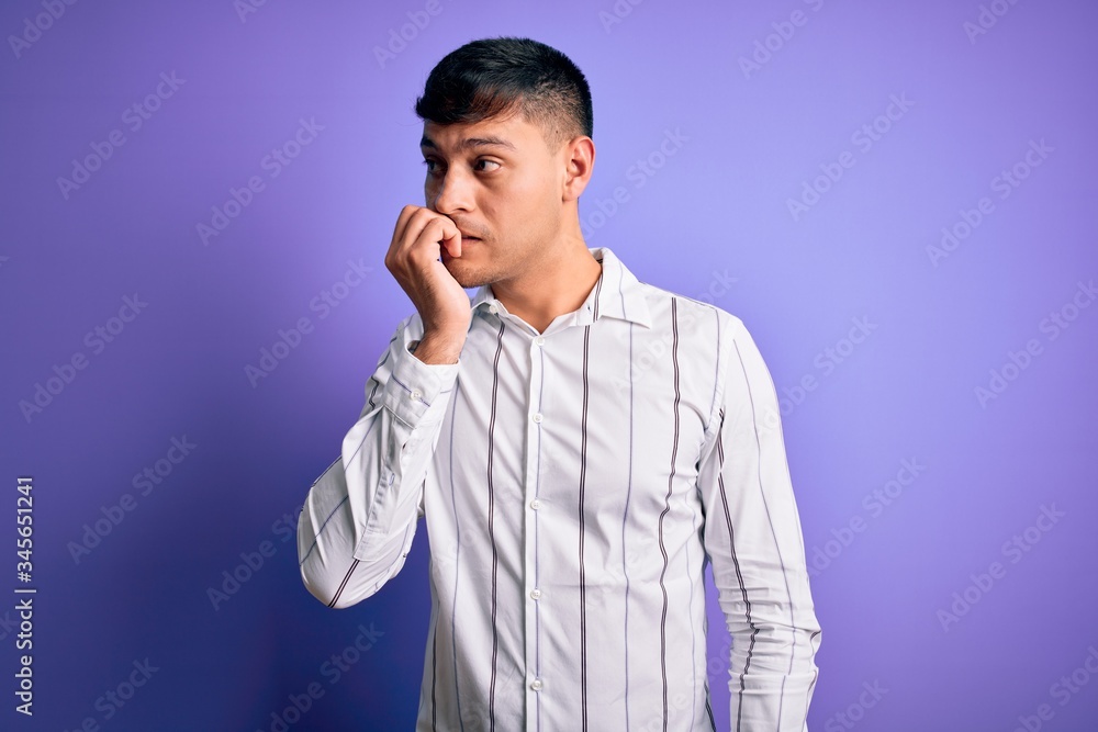 Young handsome hispanic man wearing elegant business shirt standing over purple background looking stressed and nervous with hands on mouth biting nails. Anxiety problem. Young handsome hispanic man wearing elegant business shirt standing over purple background looking stressed and nervous with hands on mouth biting nails. Anxiety problem.