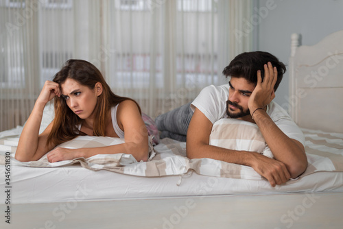 Young serious couple being angry with each other while lying on the bed