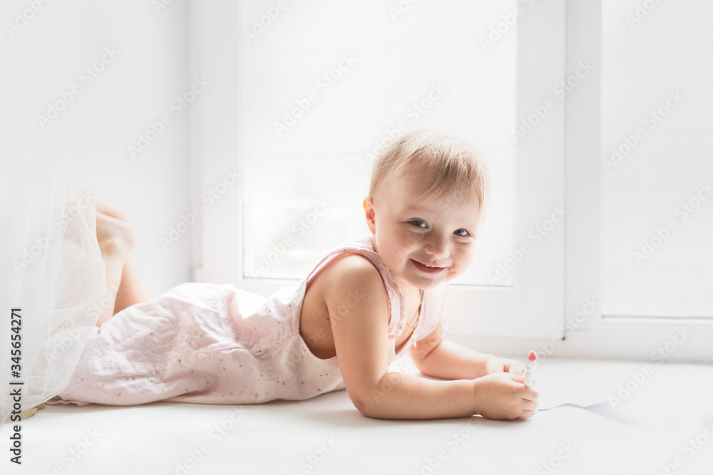 Caucasian baby girl lies and paints on windowsill Caucasian baby girl lies and paints on windowsill