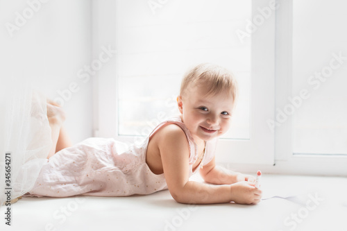 Caucasian baby girl lies and paints on windowsill